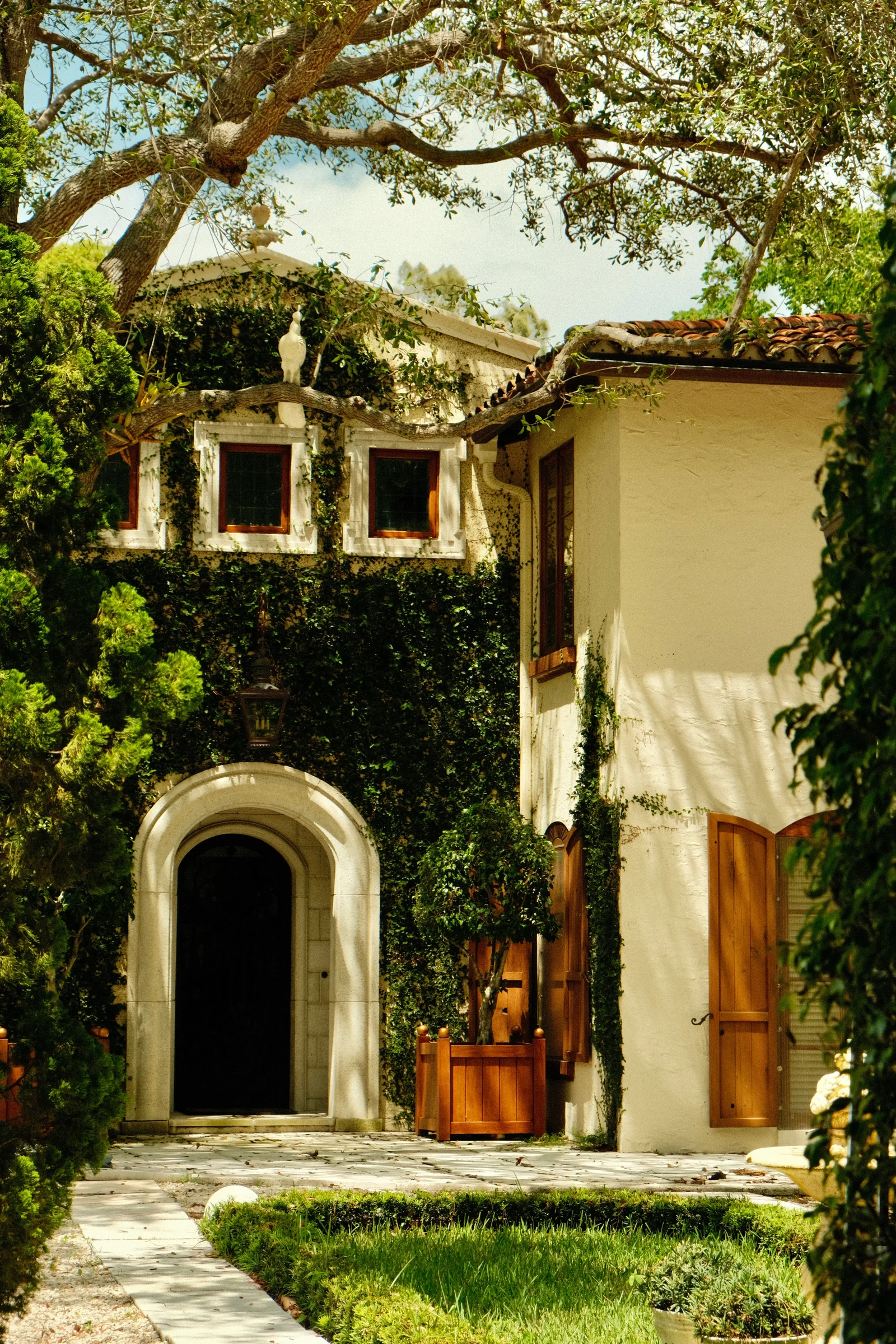 The arched front entrance of a Mediterranean-style home with ivy and wooden shutters